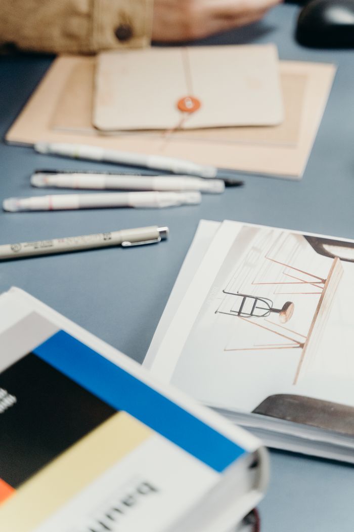 A well-organized desk featuring notebooks, pens, and a design book for creative projects.