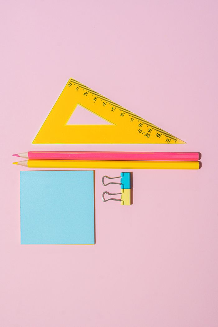 Vibrant collection of office supplies including pencils, sticky notes, and binder clips on a pink surface.